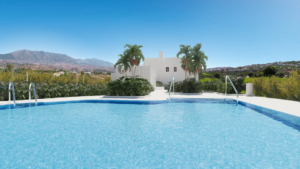 Swimming pool with clear blue water in front of a white building and palm trees against a clear sky.