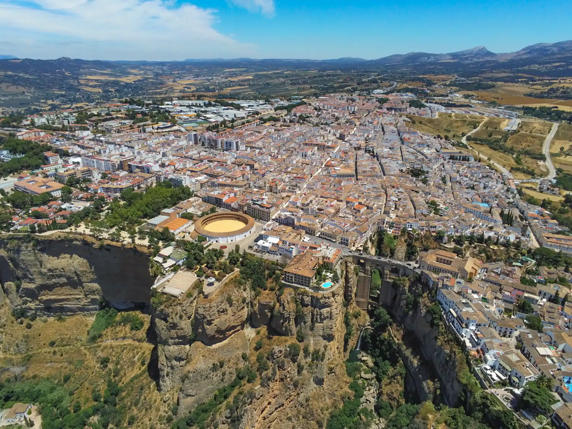 Aerial view of Ronda, Spain, showcasing the dramatic cliffs, Puente Nuevo Bridge, and historic bullring surrounded by whitewashed buildings