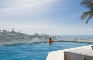 A person relaxing in an infinity pool overlooking the mediteranean and landscape.