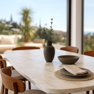 A marble dining table featuring a dark vase with branches and a bowl, accompanied by a napkin and placemat.