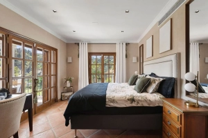 Interior view of a bedroom featuring a bed, bedside table, and window with curtains.
