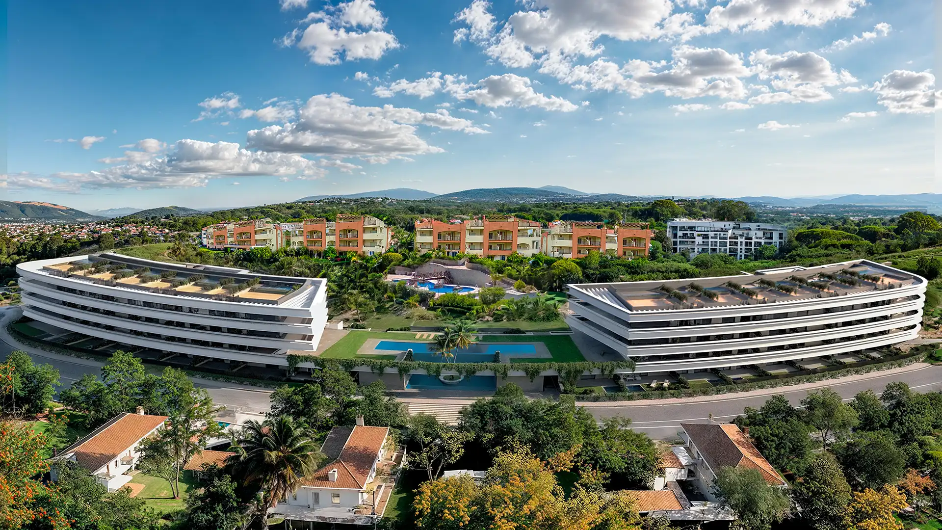 Aerial view of a modern residential complex featuring landscaped gardens and a swimming pool.