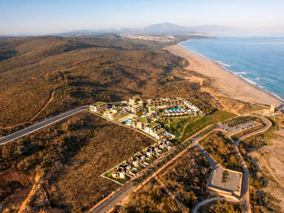 Aerial drone shot showing modern luxury resort with multiple buildings, pools and villas near pristine beach coastline