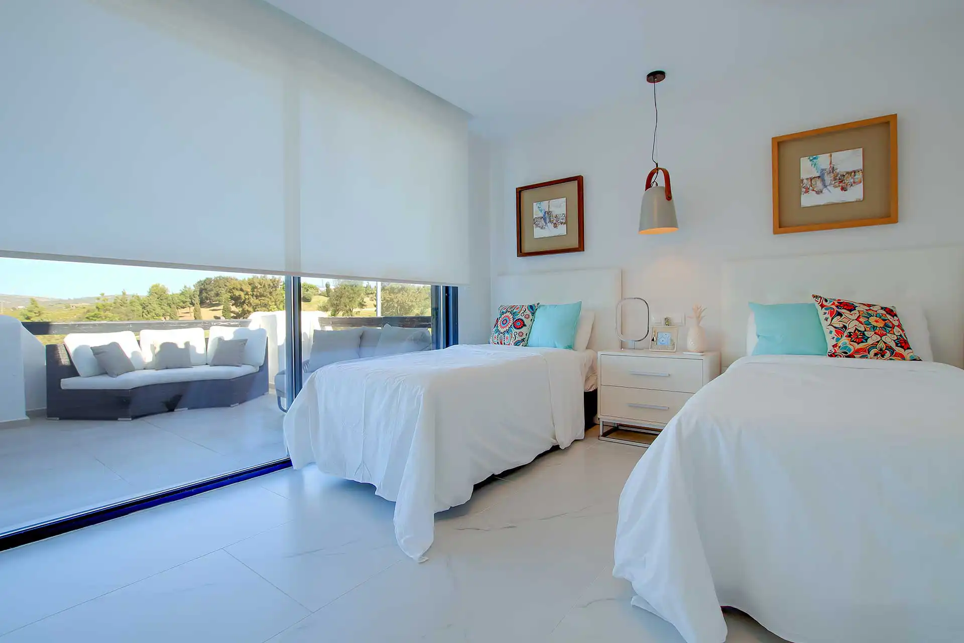 Bright modern twin bedroom with white bedding, colorful pillows, floor-to-ceiling sliding doors opening to a terrace with panoramic golf course views