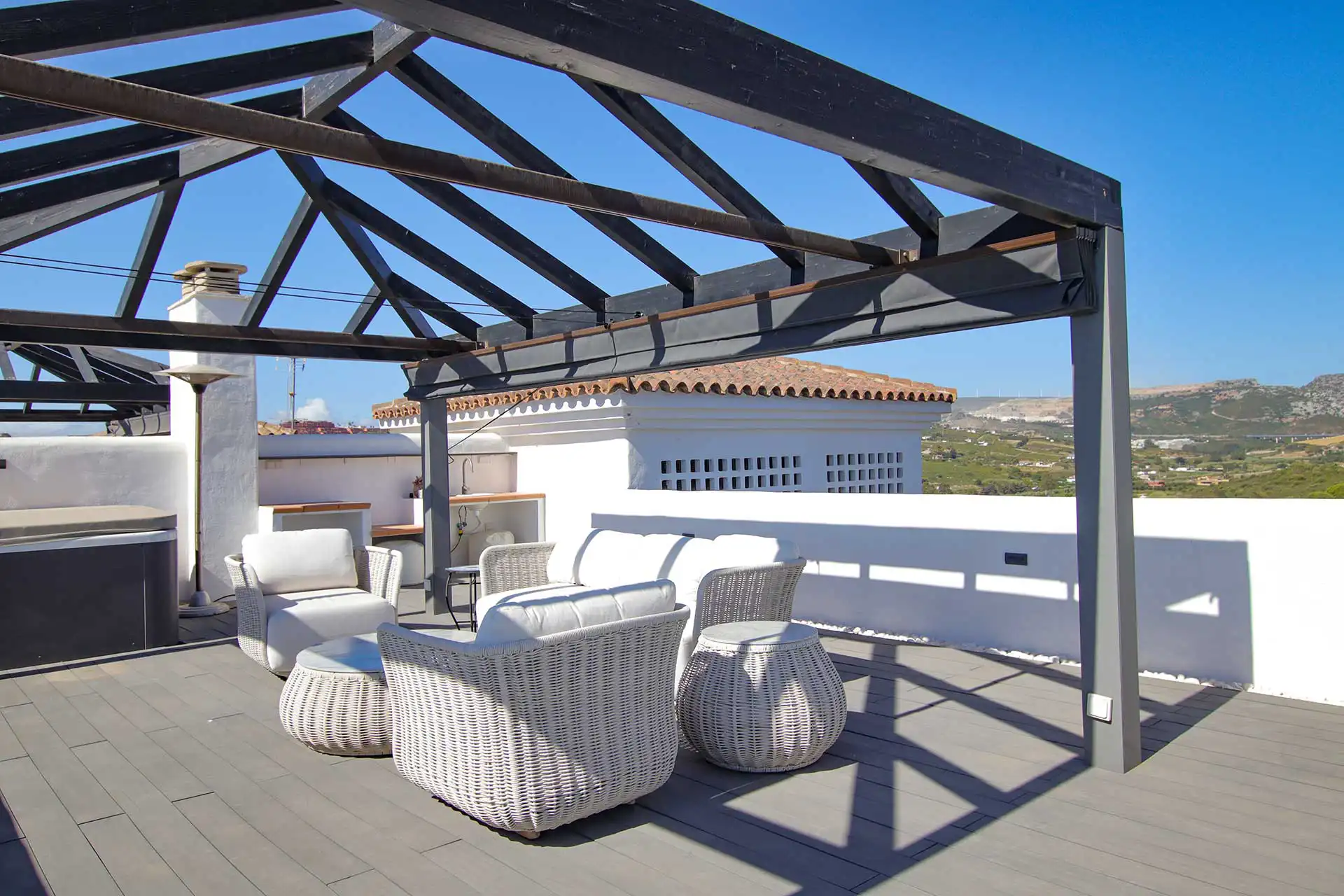 Stylish rooftop terrace at Lotus Dona Julia featuring a dark steel pergola, white wicker lounge furniture, and panoramic mountain views