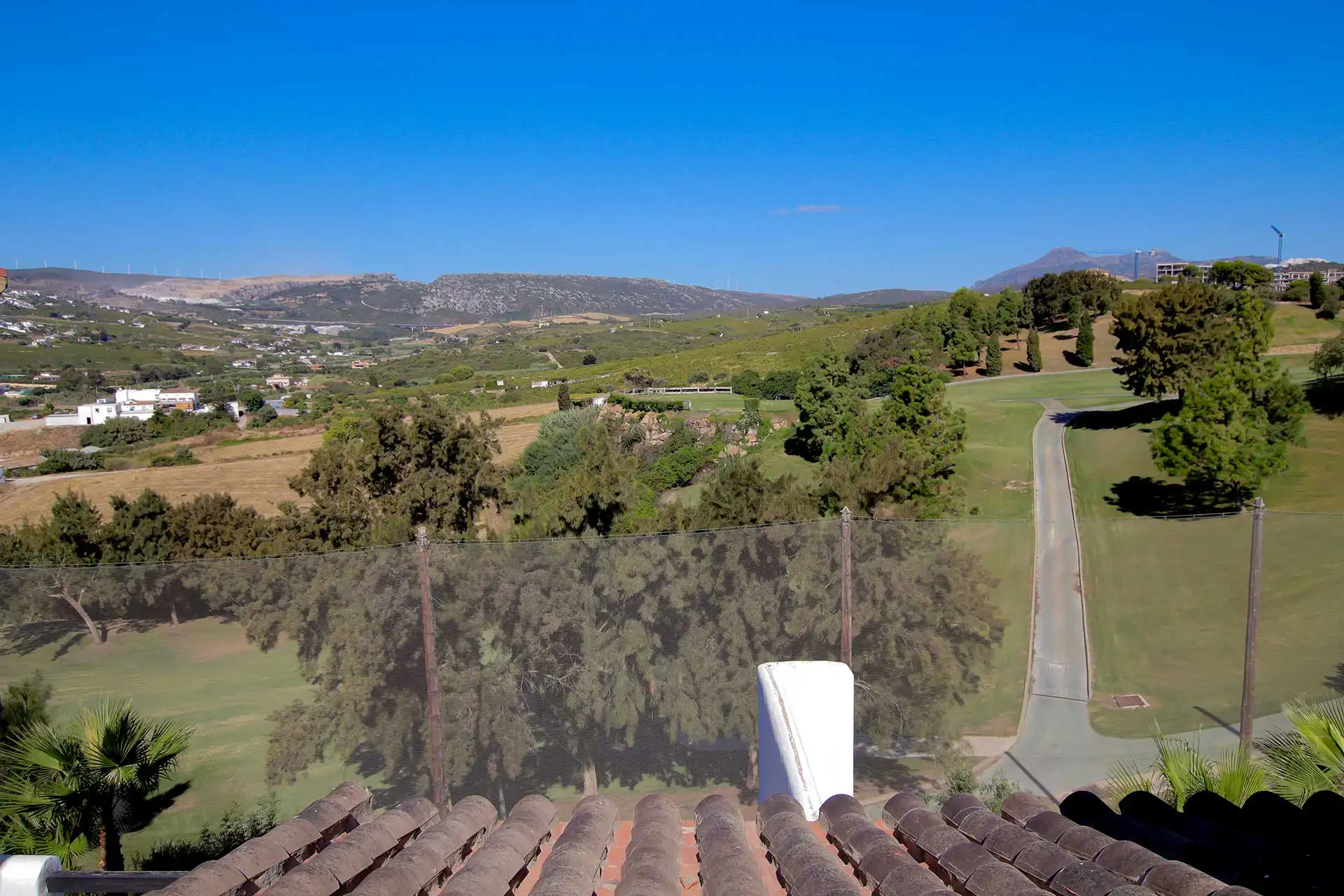 Elevated rooftop terrace view overlooking lush golf course fairways, pine trees, and rolling mountain landscape in southern Spain