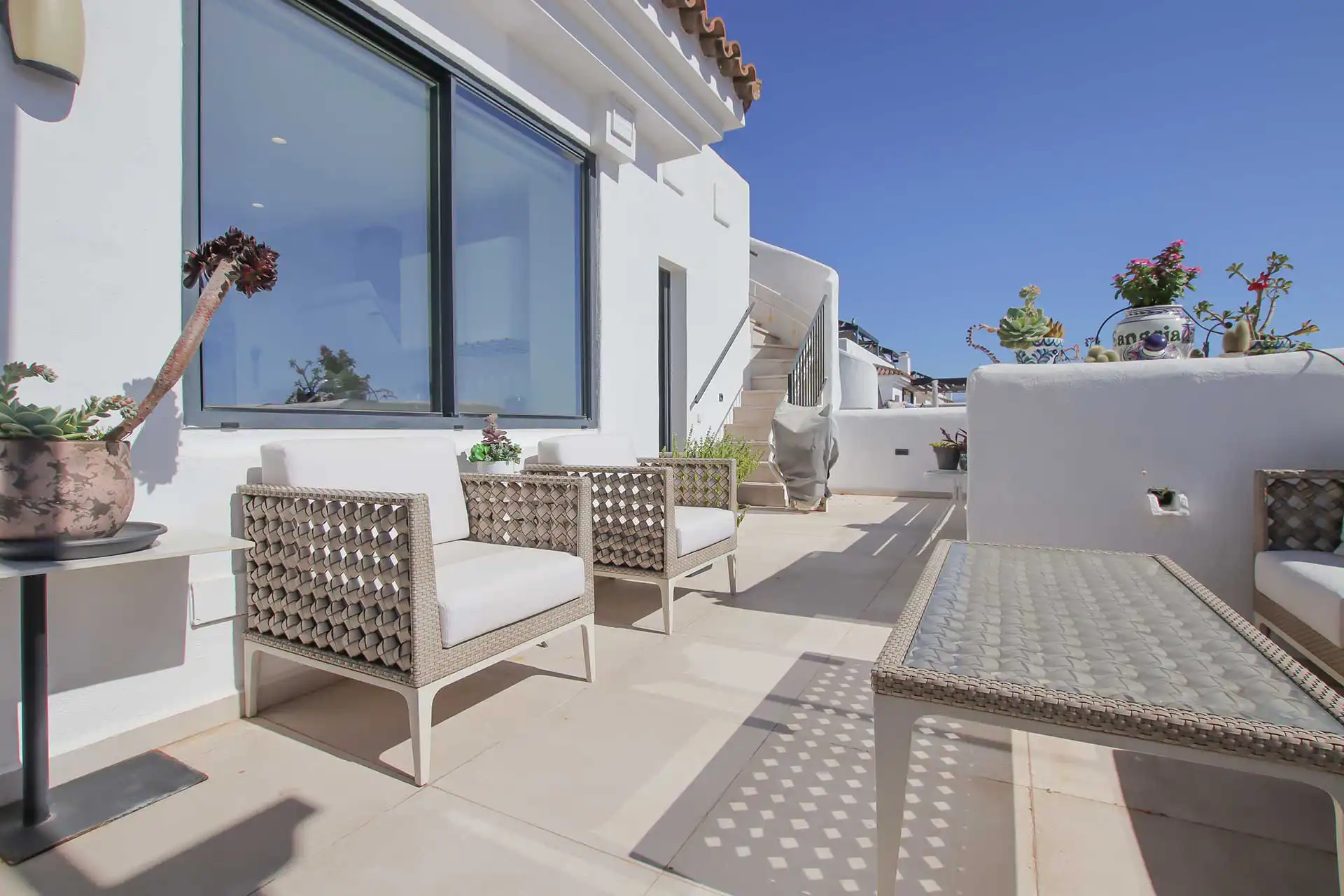 Spacious rooftop terrace at Lotus Dona Julia with woven rattan armchairs, white cushions, and potted succulents under a clear blue sky