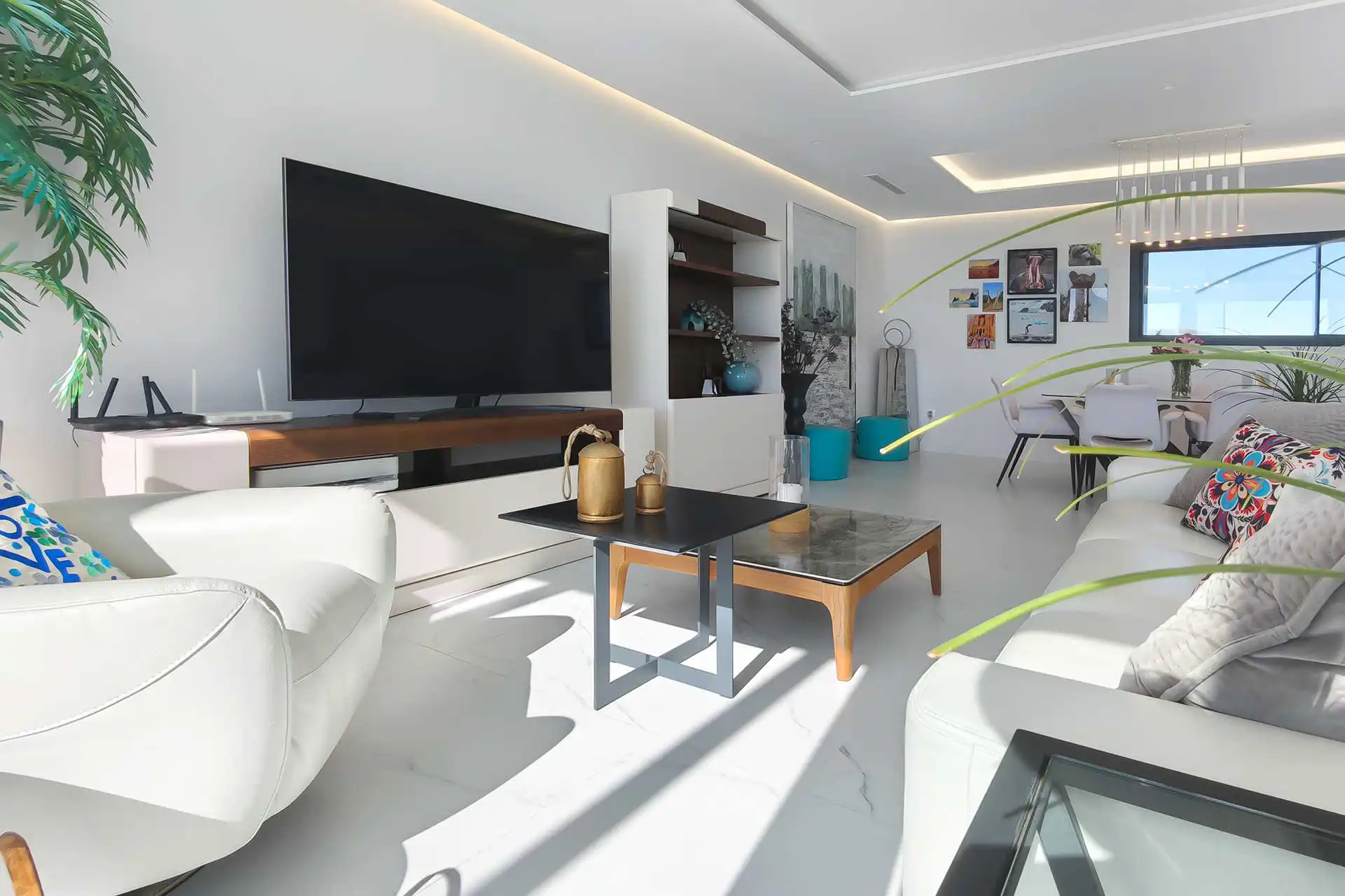 Bright open-plan living room with white leather sofas, large flat-screen TV, marble floors, and dining area with sea views