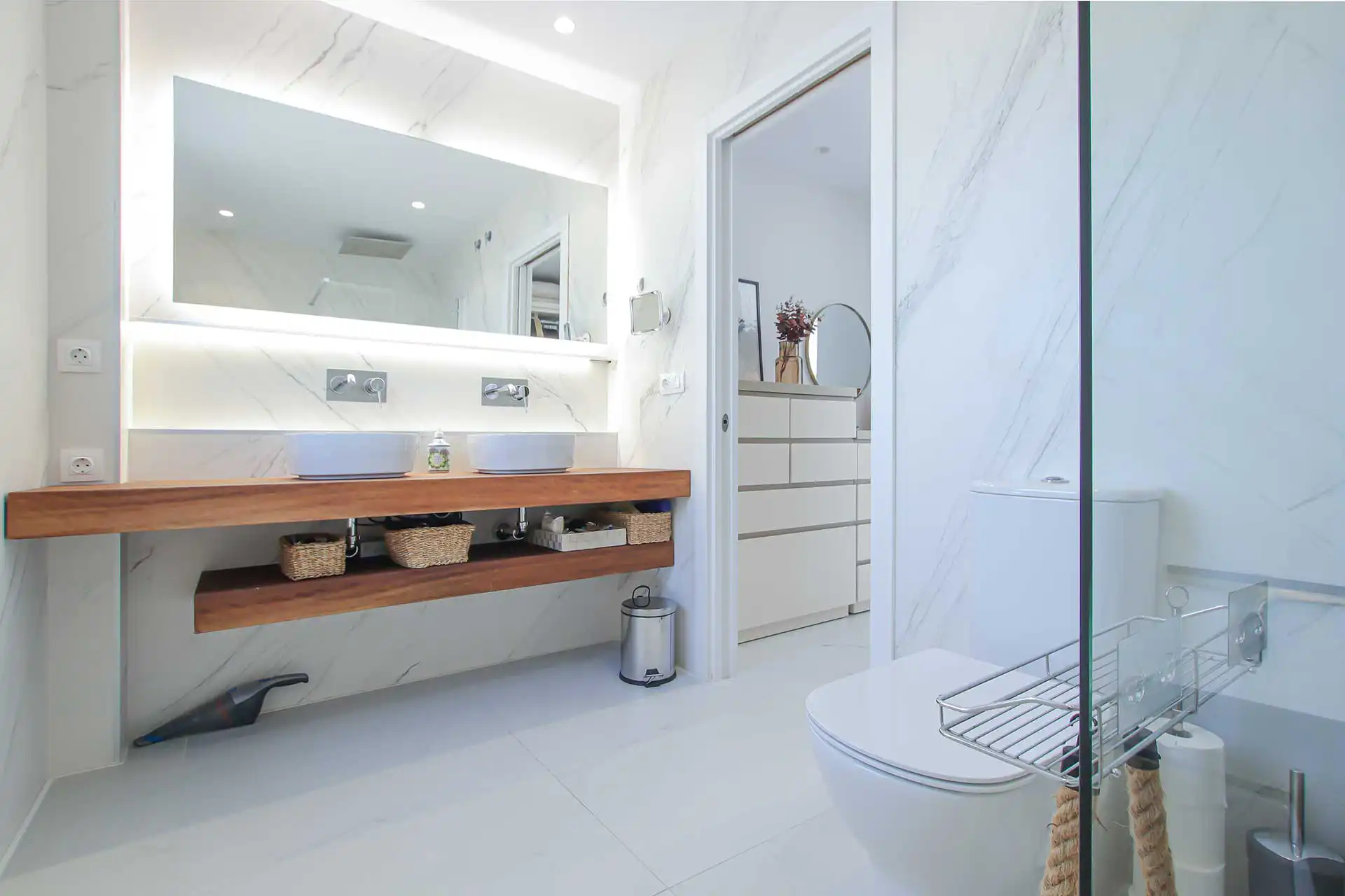 Modern luxury bathroom featuring double vessel sinks on walnut floating vanity with backlit LED mirror and marble walls
