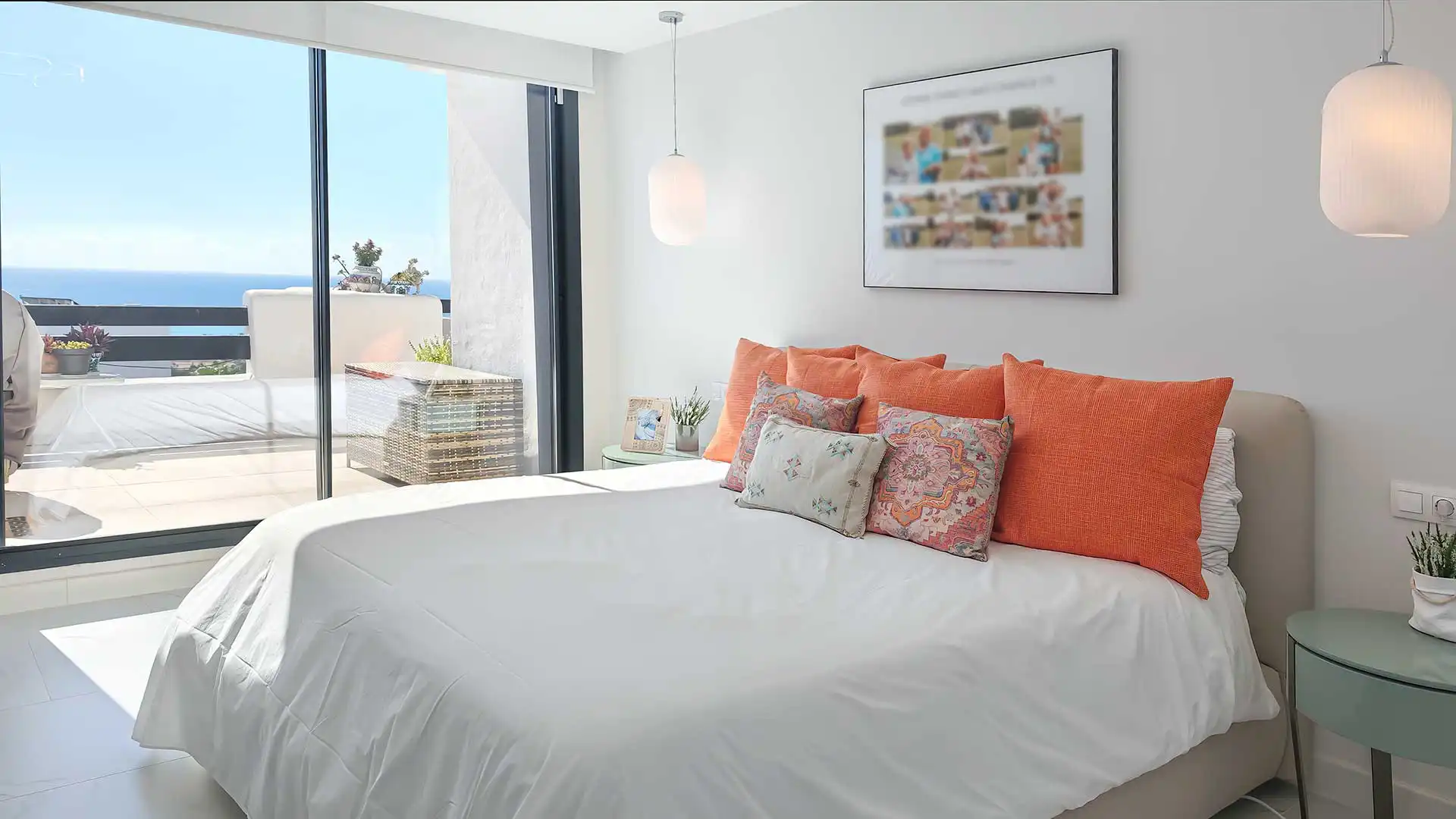 Modern white bedroom with orange accent pillows, floor-to-ceiling sliding doors opening to a sun-drenched terrace with ocean views